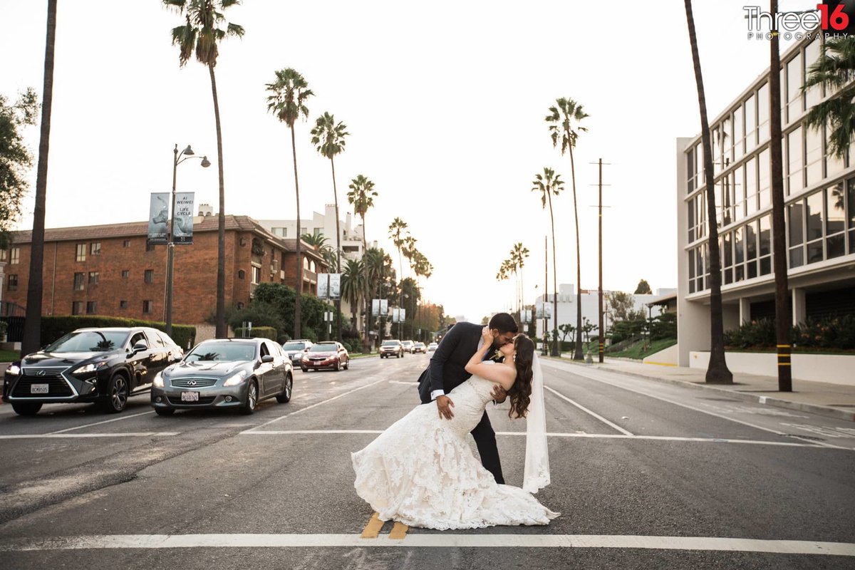 Groom dips and kisses his Bride in the crosswalk of a busy street in Los Angeles in front of stopped cars