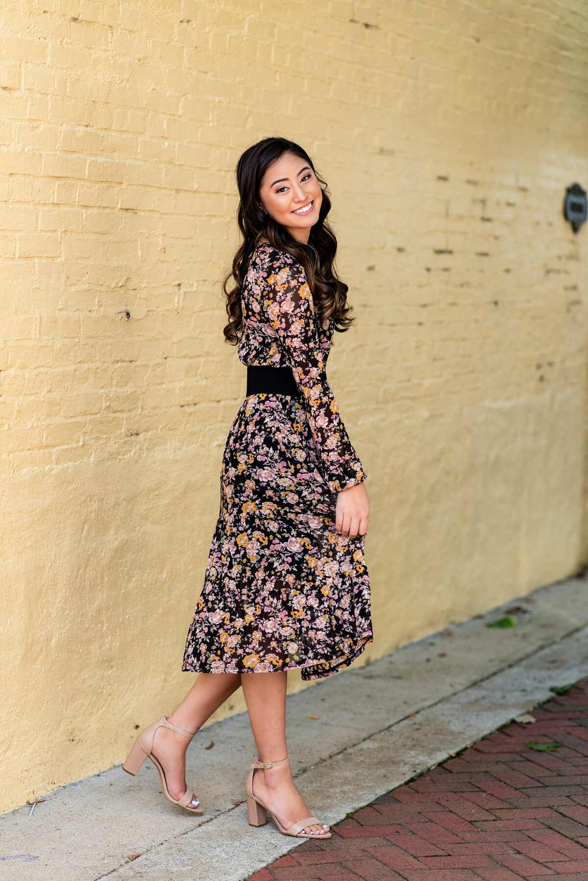 Richmond, VA senior girl poses on sidewalk in Uptown Richmond, VA wearing floral dress.