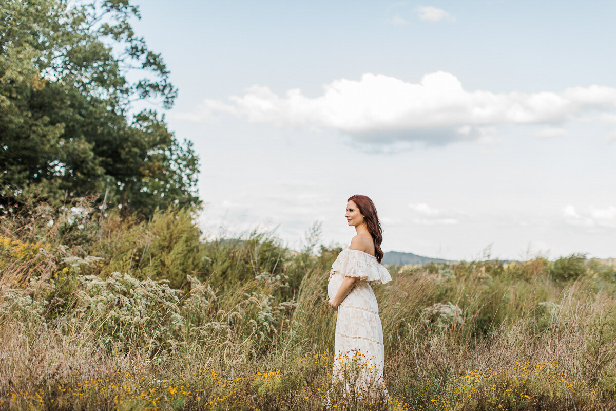 scenic maternity portrait of mom standing in a wild flower field with wind blowing her hair
