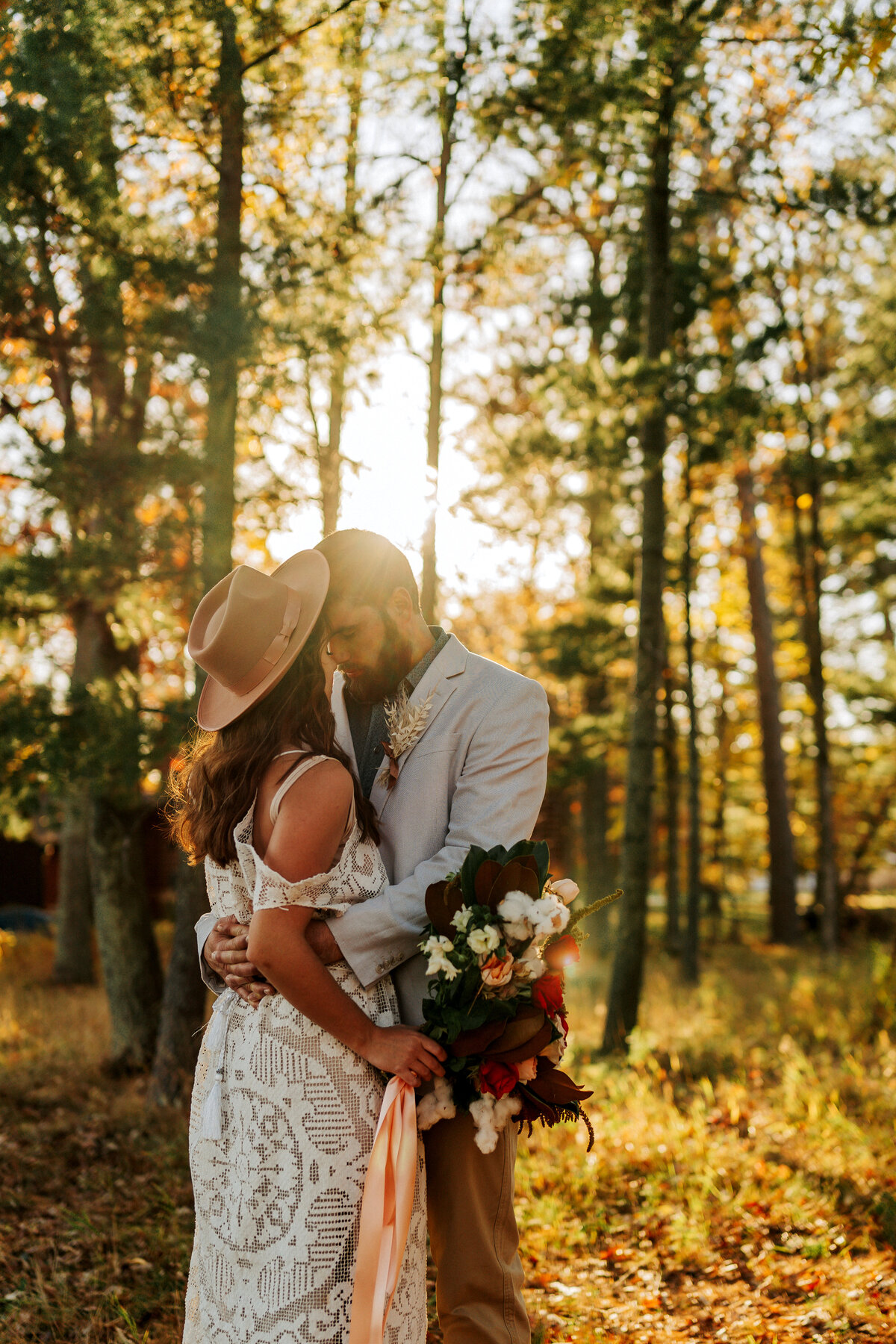 married couple hugging at sunset with bouquet of flowers
