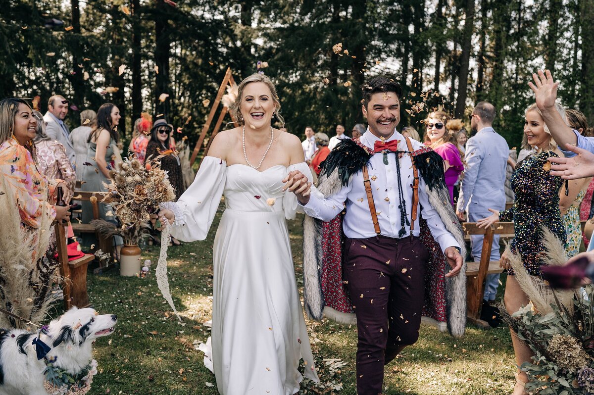 bride wearing removable sleeves and groom with korowai walk out of forest ceremony while guests throw confetti in woodbury geraldine