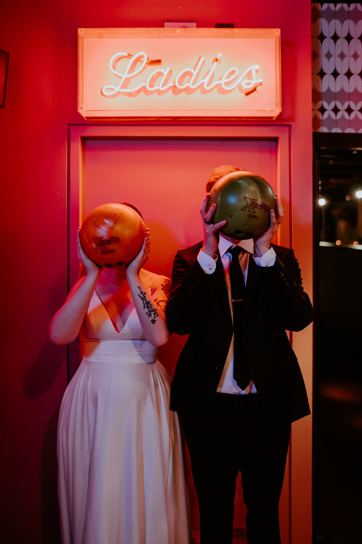 A couple hold bowling balls to their faces at Seven Stars Bowling Ally in London. They wanted alternative wedding photography and had awesome wedding ideas to make cool wedding photos.