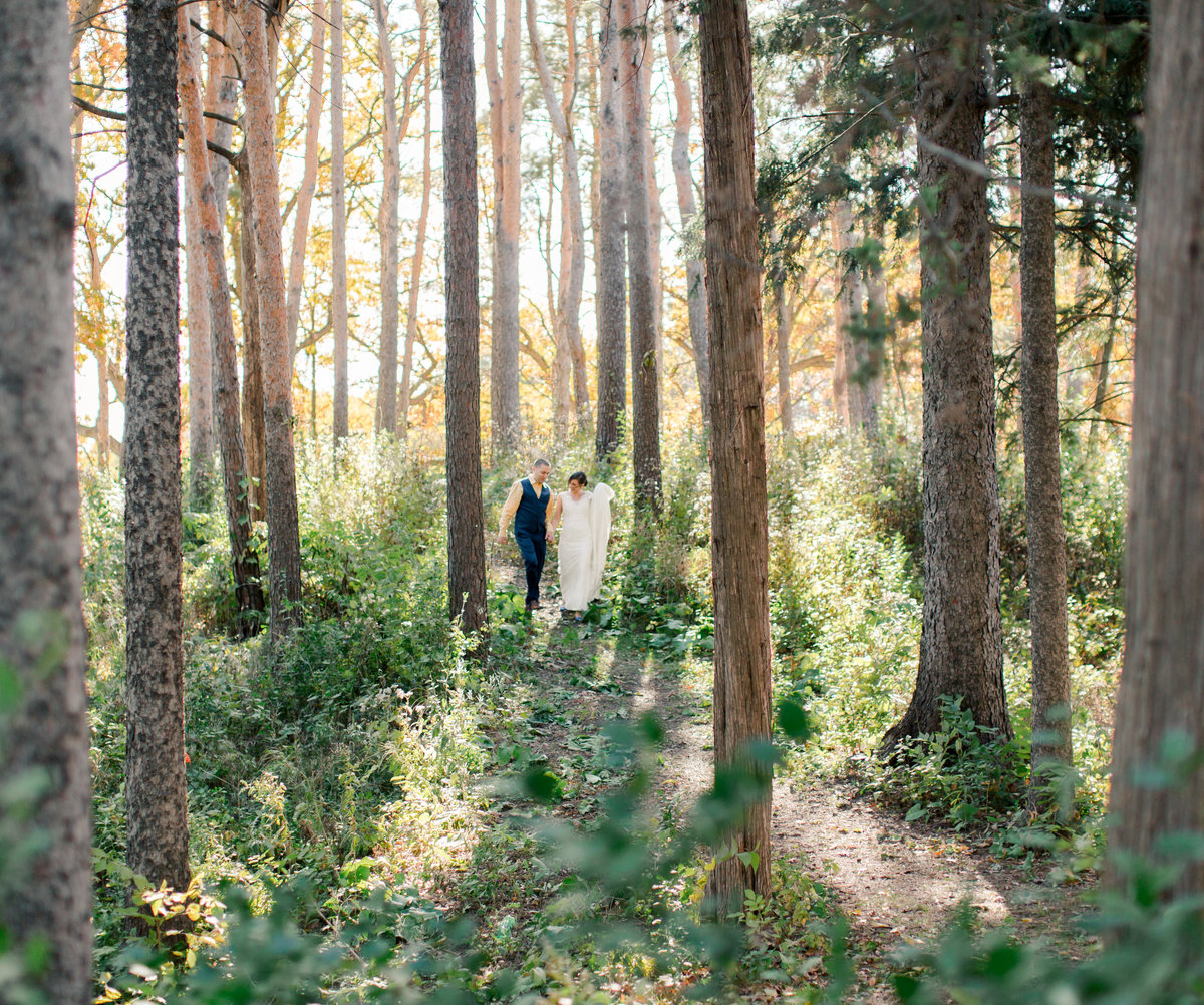 among tall pines in the fall bride and groom walk together through the forest