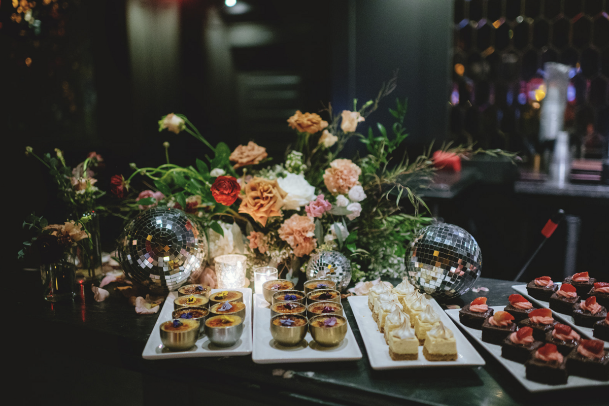 Lush roses, greenery and disco balls decorate dessert buffet at trendy Holly Blue wedding reception in Fort Lauderdale, Florida.