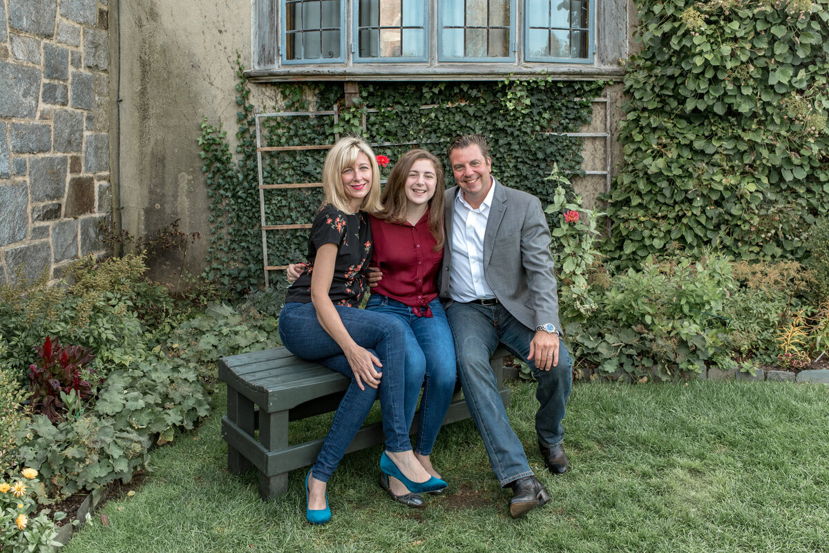 Family of three sitting on bench in garden with mansion
