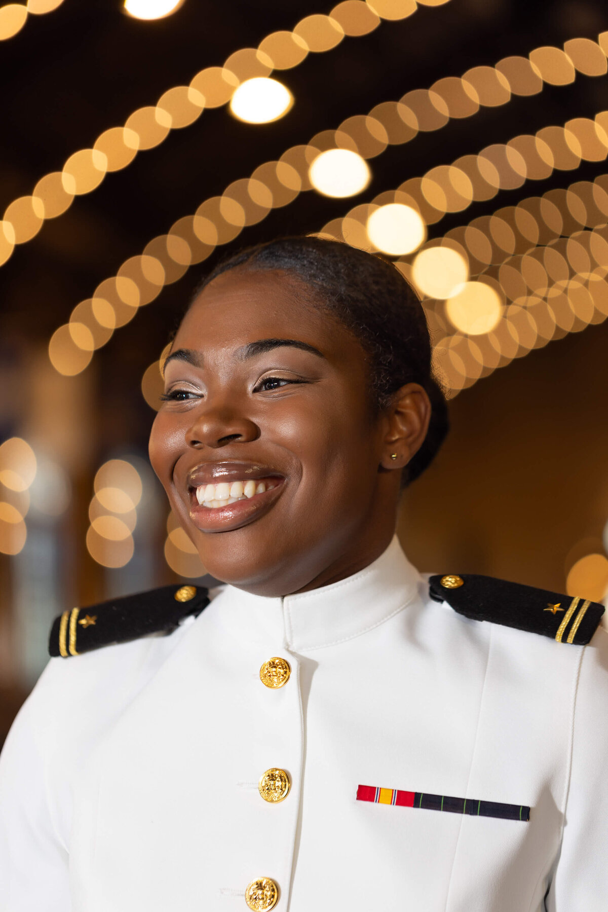 Female Naval Academy graduate smiling profile with bokeh lights.