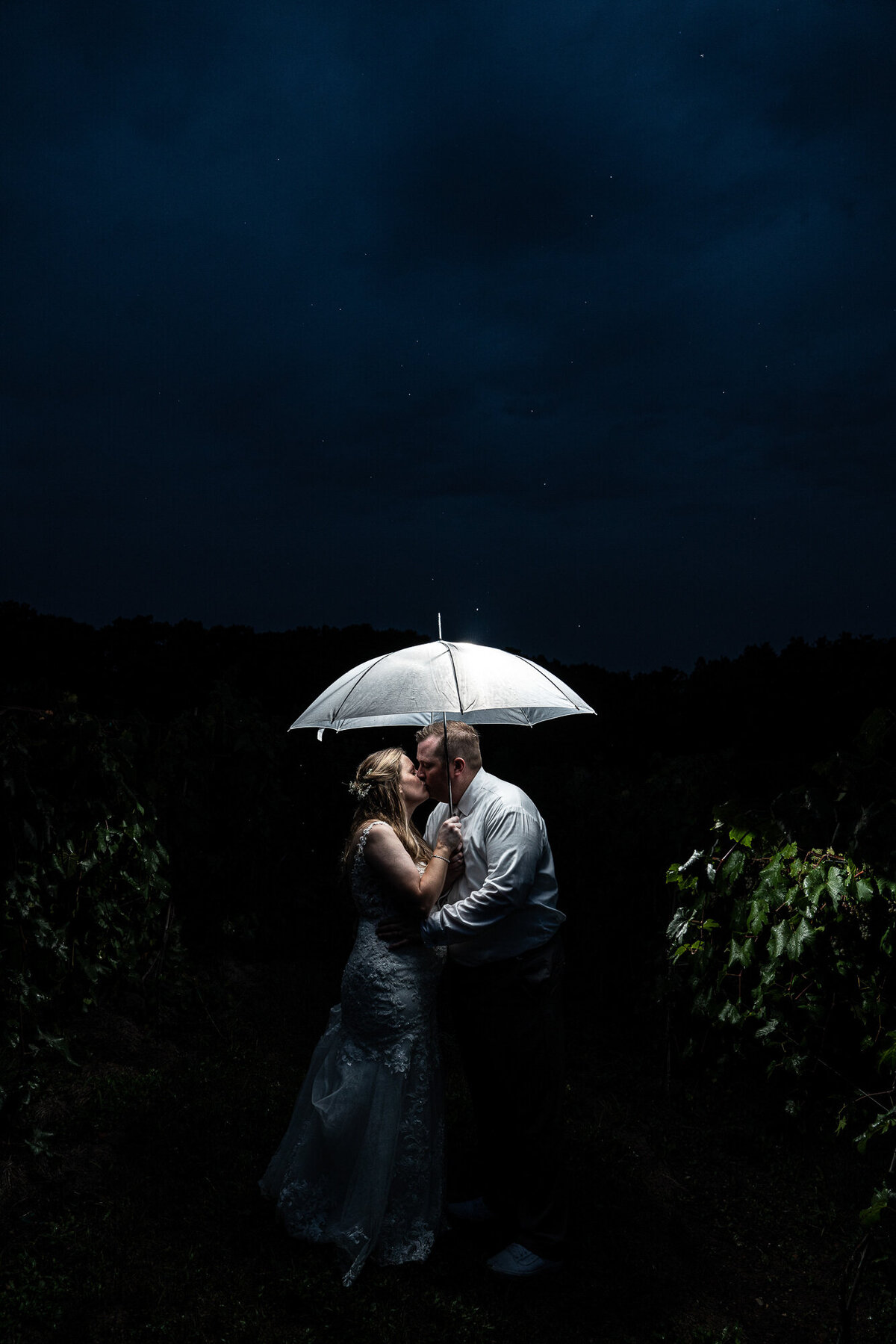Bride and groom kiss under umbrella at night.