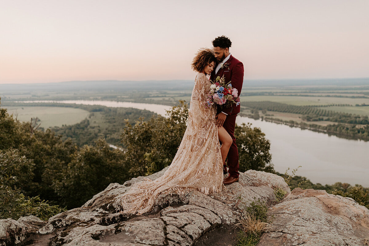 An eloping couple embrace on a cliffside at Stouts Point, Petit Jean State Park. The Arkansas River can be seen in the valley below in the background.