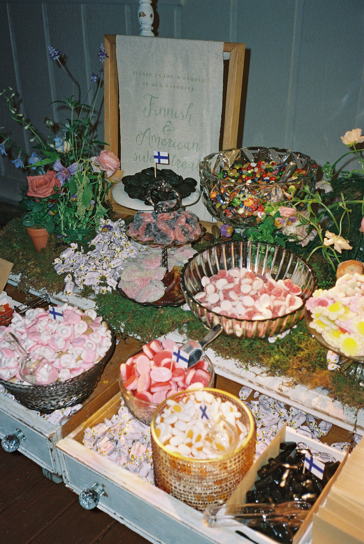 Film photograph of a whimsical candy bar filled with Finnish and American sweets, styled with moss, wildflowers, and garden-inspired florals for a playful wedding reception in Northwest Arkansas.