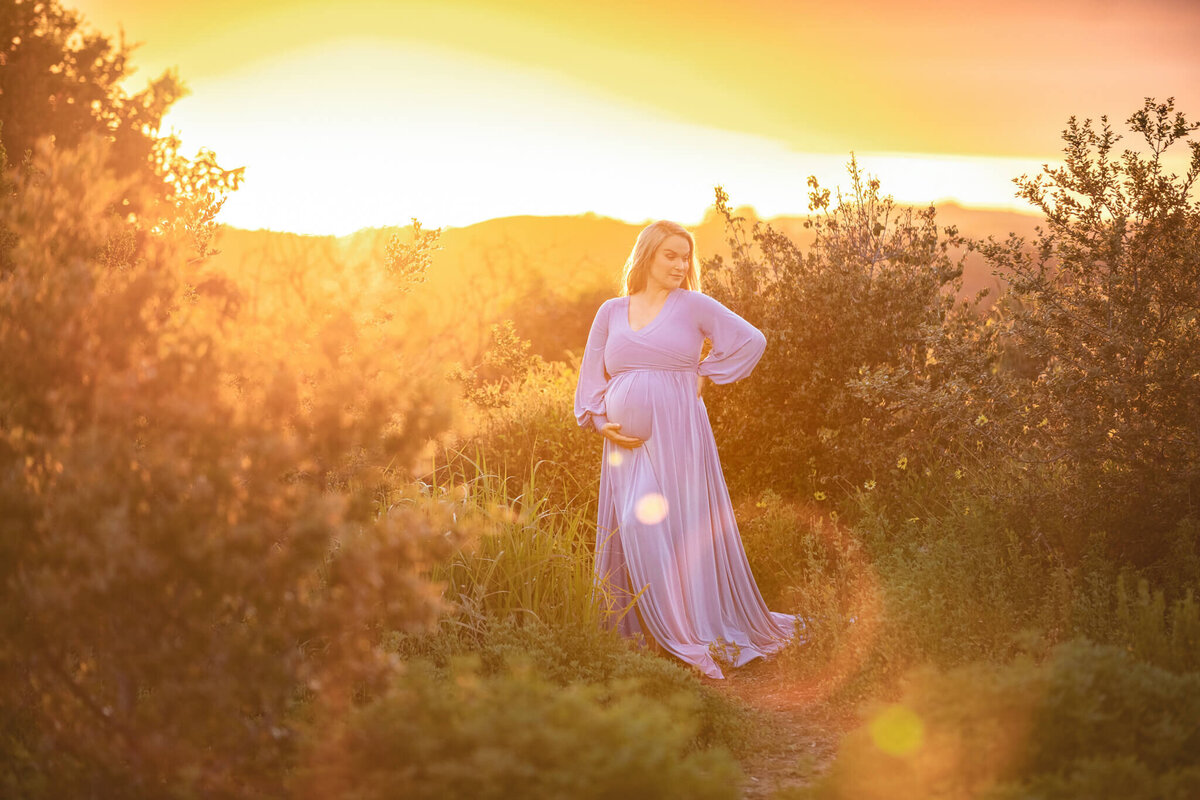 Sunset maternity image photographed in Woodland Hills. Mom wearing a blue dress and surrounded by a soft glowing sunset