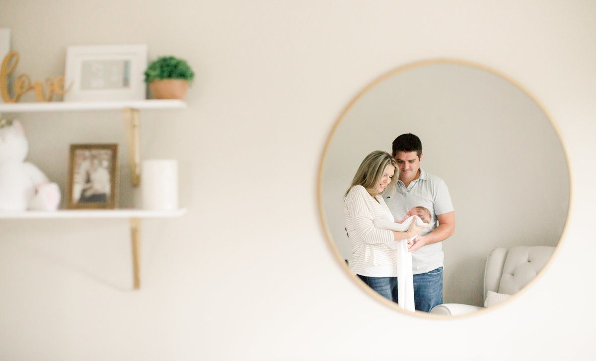 mom and dad holding daughter in reflection of circle mirror in nursery of home
