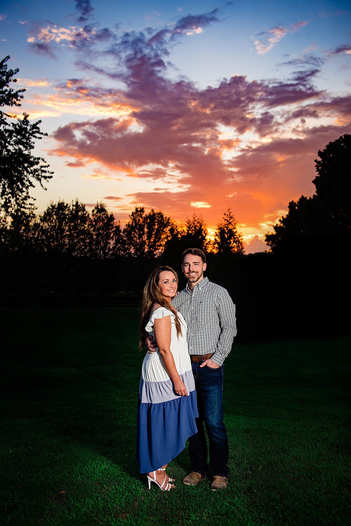 Bright Orange, Purple and Blue sunset with engaged couple standing together and smiling at the camera