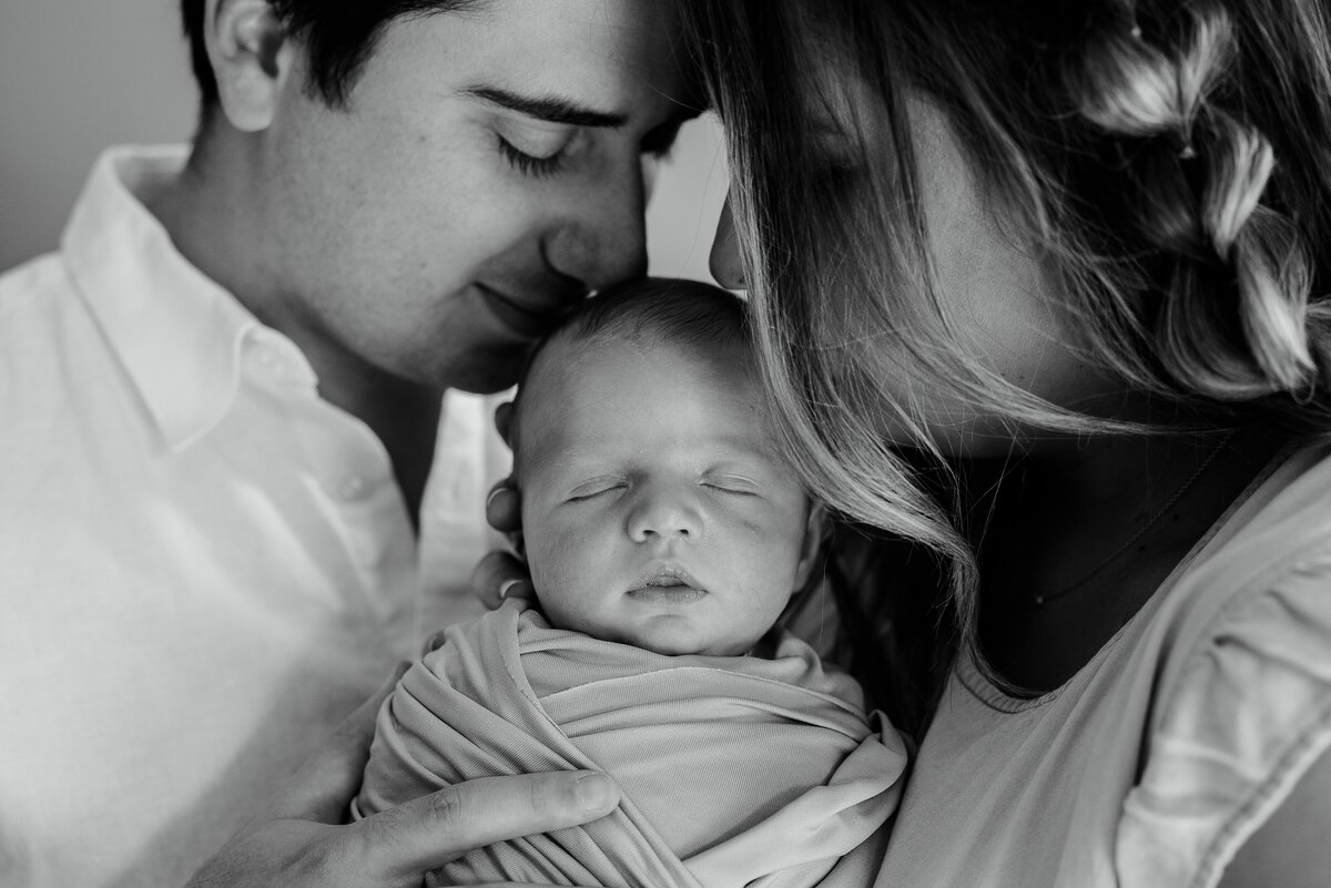 Mother and father kissing newborn