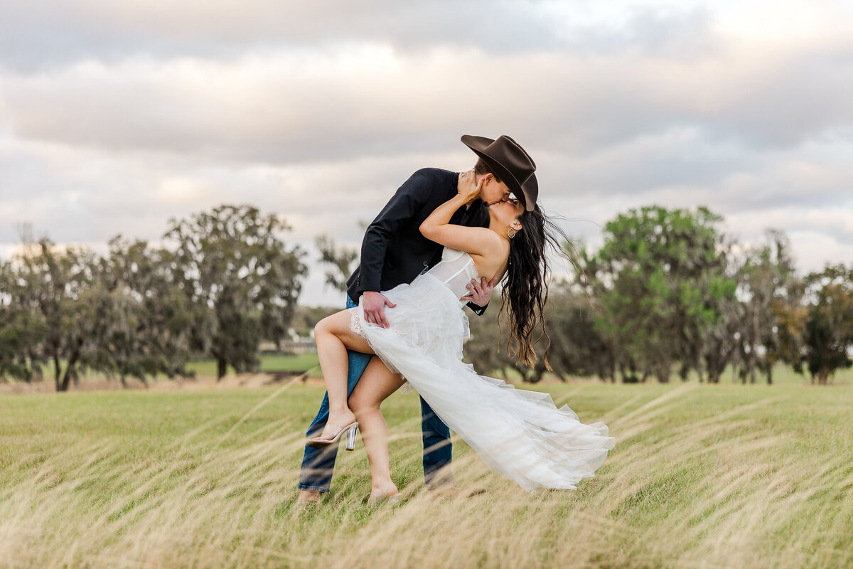 A man dips and kisses a girl in a white dress in a field and with the wind blowing at Covington Farm in Florida.