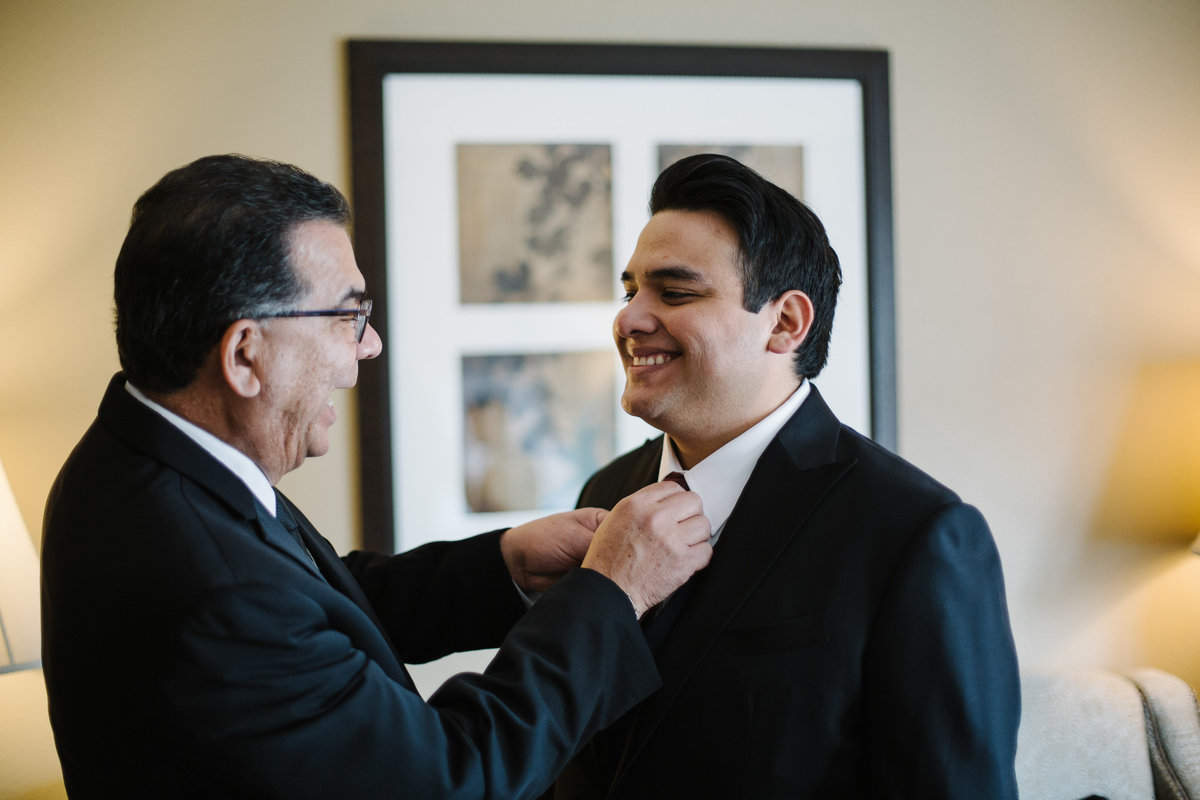 father of groom adjusts grooms tie as they get ready for wedding ceremony in downtown san antonio