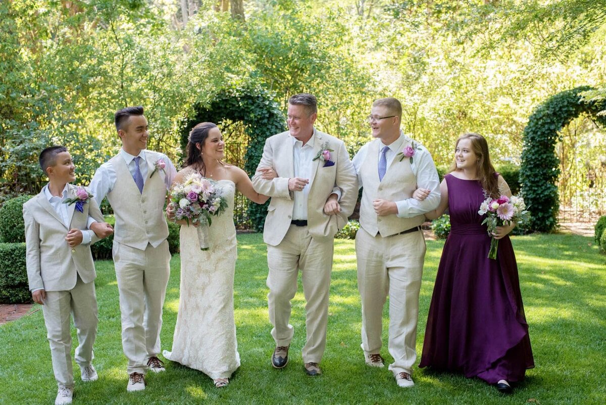 a wedding party linking arms walk through the garden at deepwood house