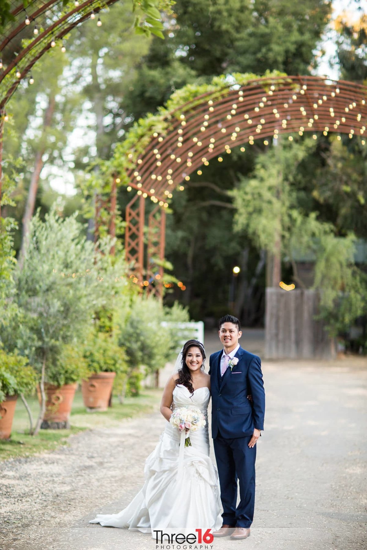 Bride and Groom stand next to each other as they pose for photos under the large archway at the Calamigos Ranch