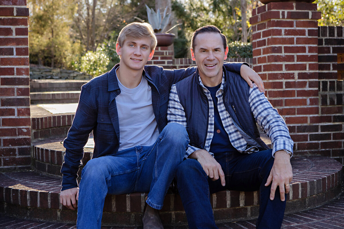 Confident father‑son portrait on brick terrace steps in autumn at UNCC Botanical Garden Charlotte NC