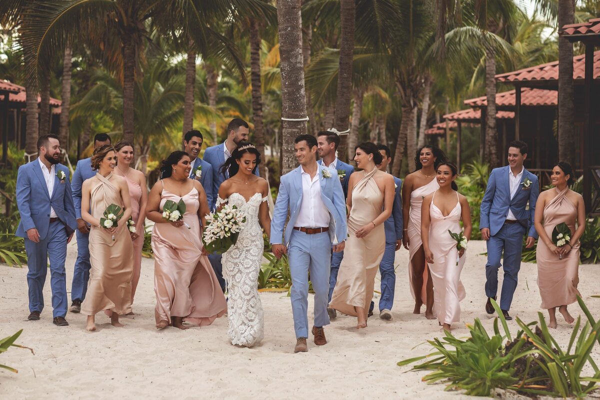 Wedding party walking on beach with palm trees in background at wedding in Riviera Maya.