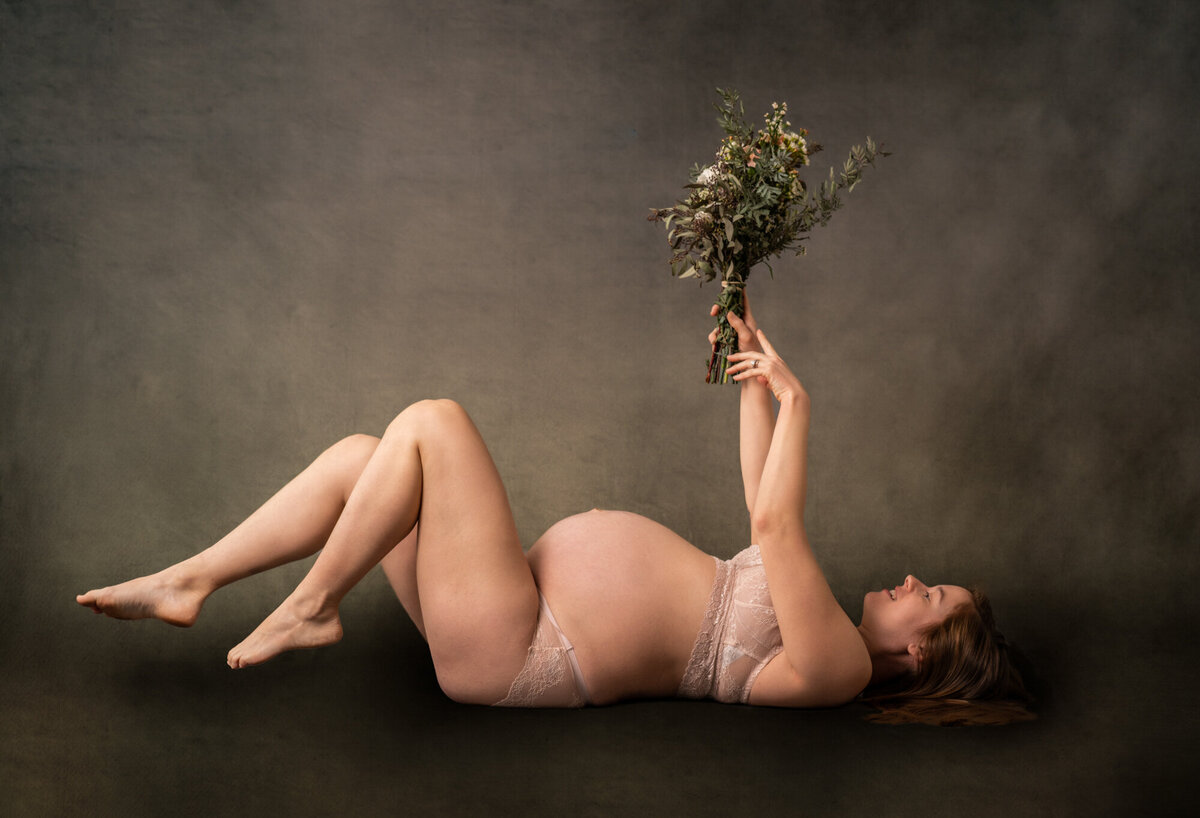 A mama to be holds flowers above her while laying on her back