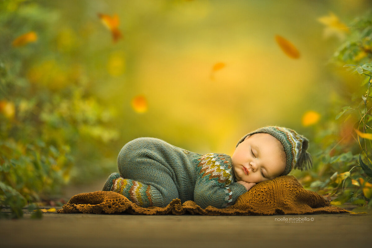 Baby in sage knits sleeping on wooden boardwalk in autumn.