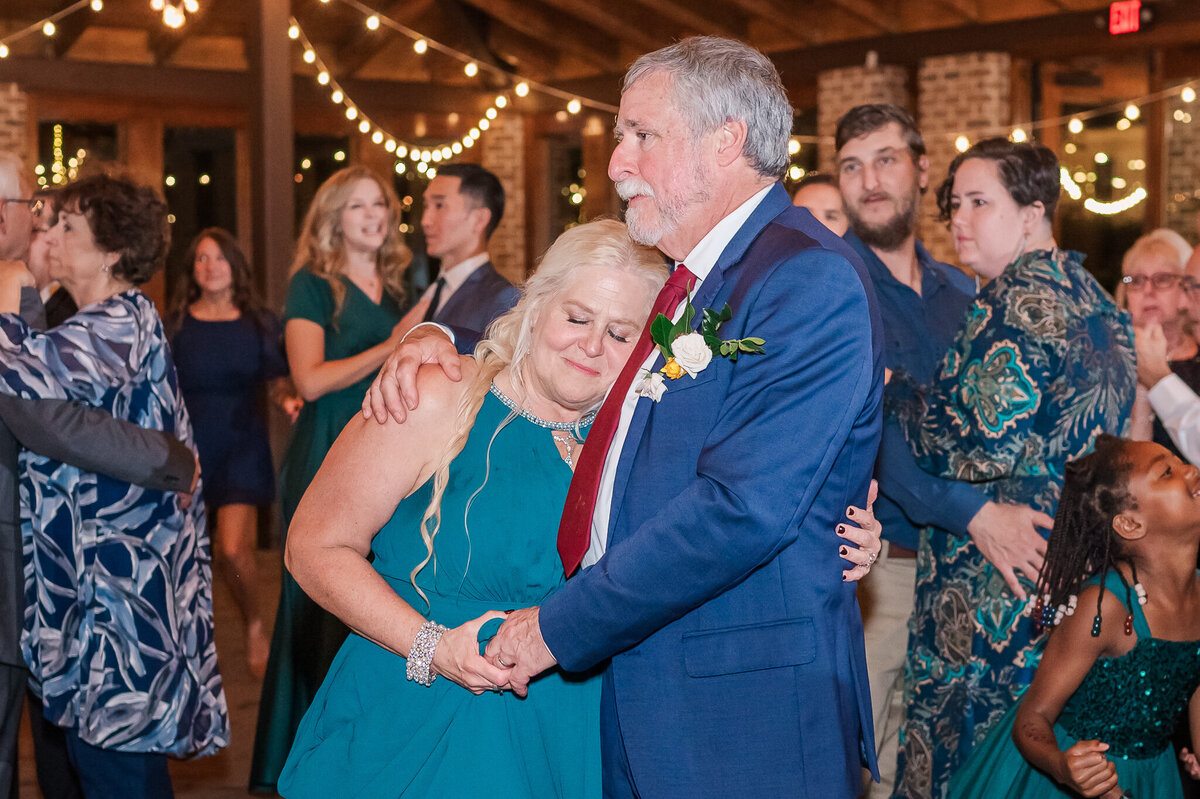 The mother and father of the bride holding each other during a wedding reception enjoying their Raleigh wedding photography session by JoLynn Photography