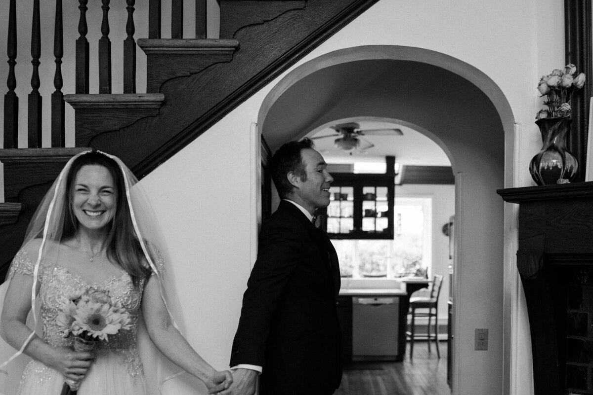 Bride and groom in a white wedding gown and black tuxedo holding hands near a staircase.