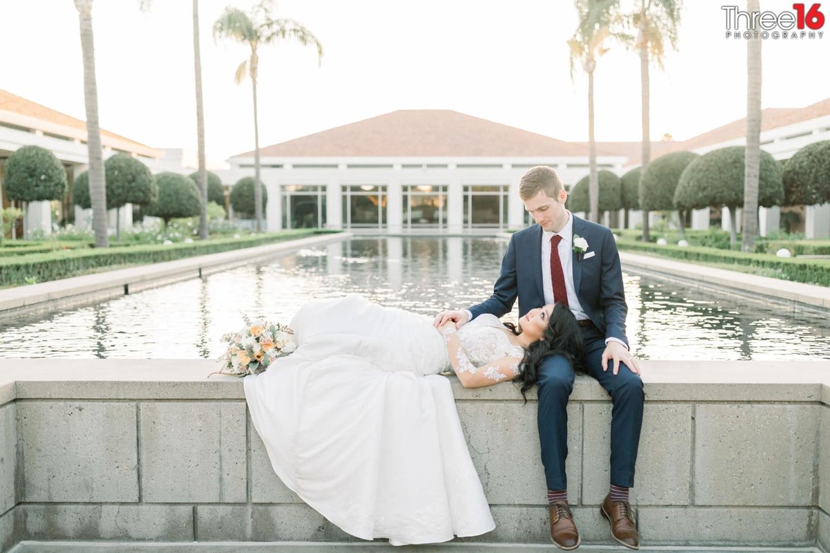 Bride rests her head on Groom's leg next to the Richard Nixon Library's Reflecting Pool