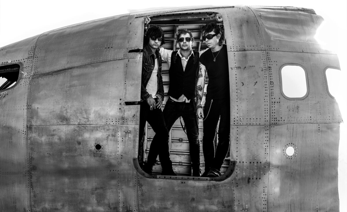 Musical trio portrait Dead Day Revolution black and white standing looking out old metal plane doorway