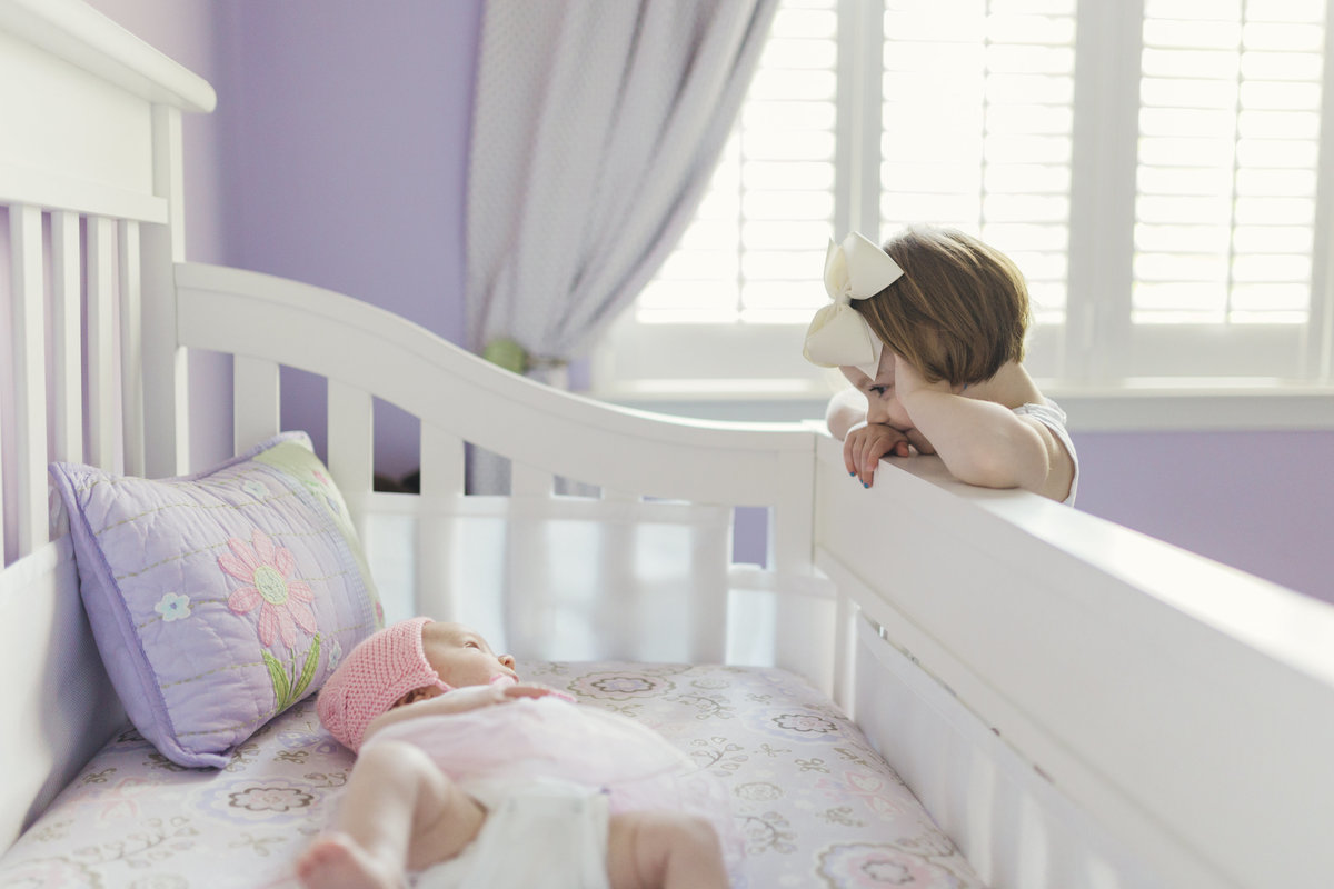 charlotte family photographer creates a beautiful lifestyle image of big sister looking over the crib at the new baby