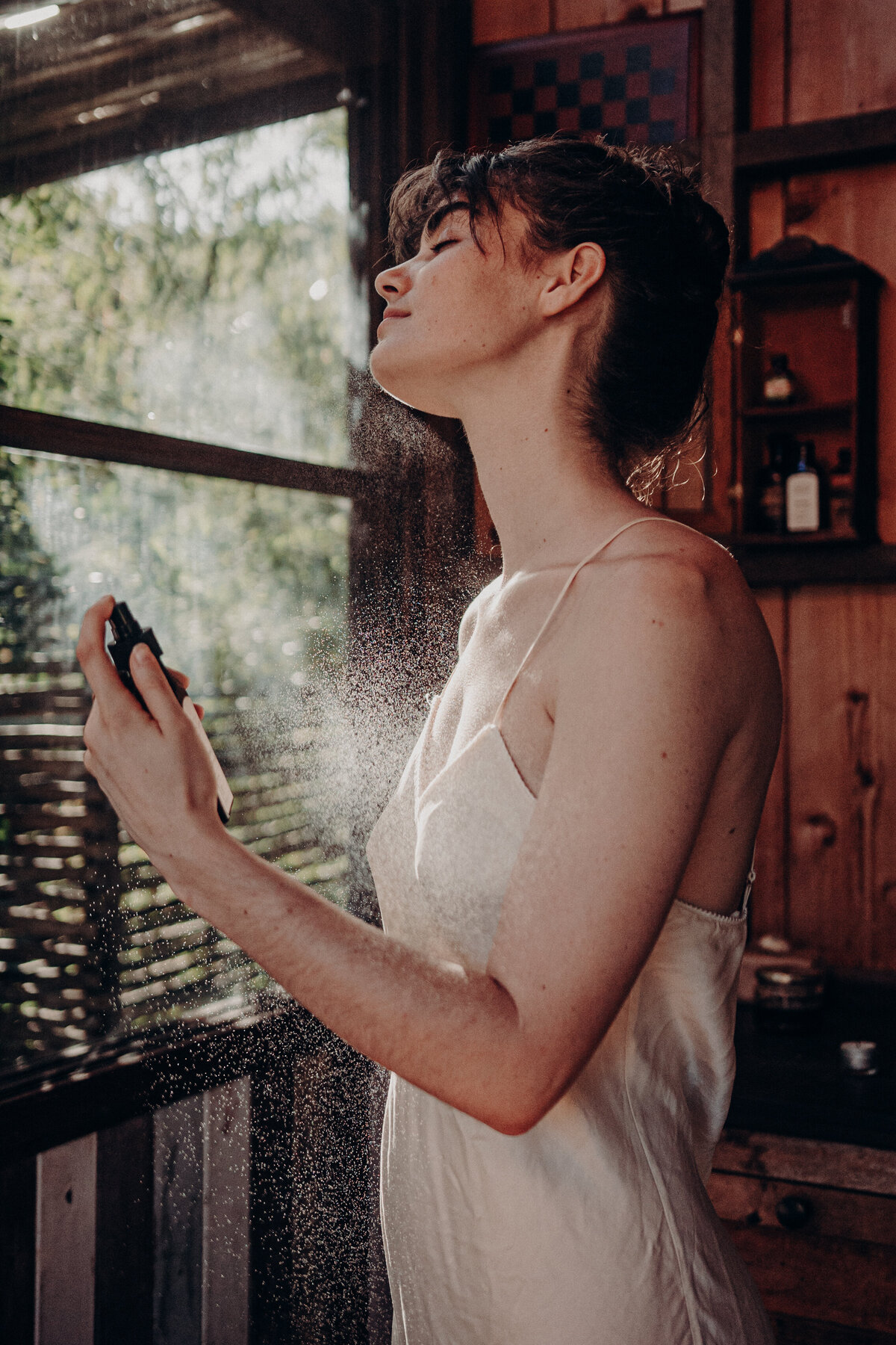 Female model spraying oil on her skin.