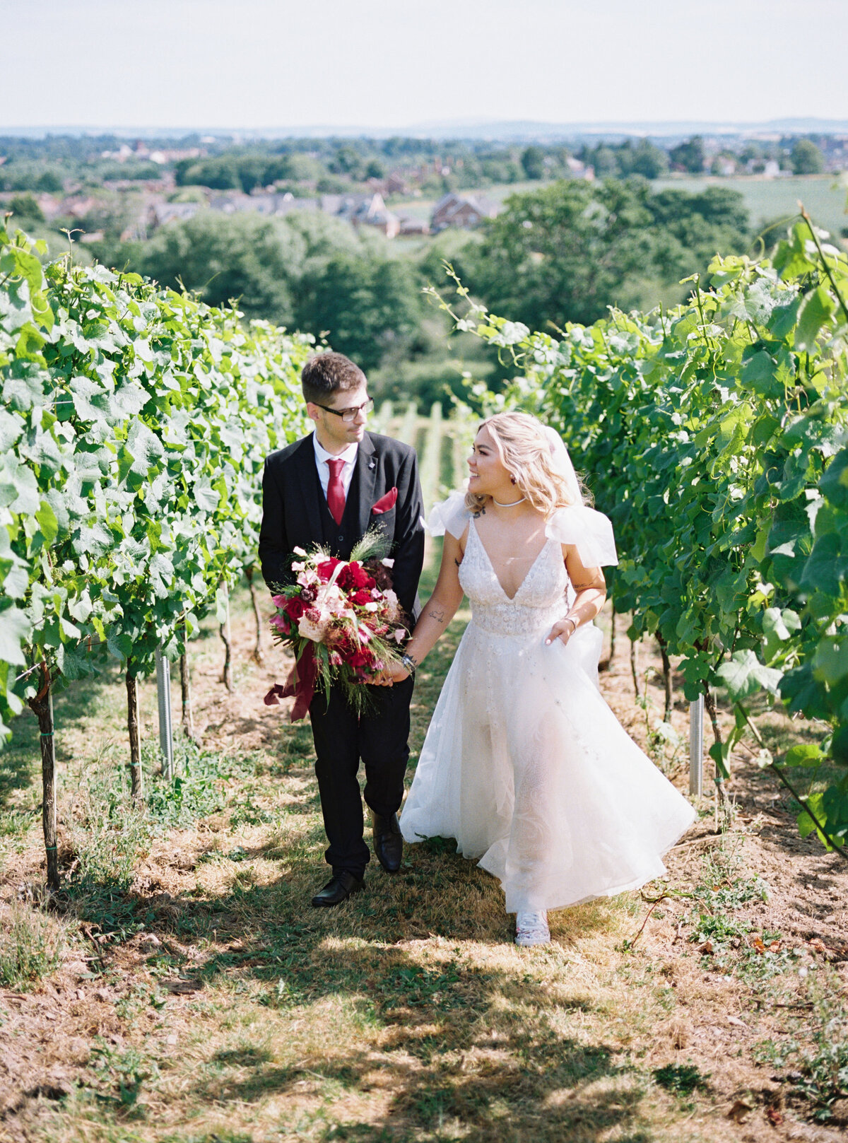 bride and groom holding hands and looking at each other smiling walking between vineyards