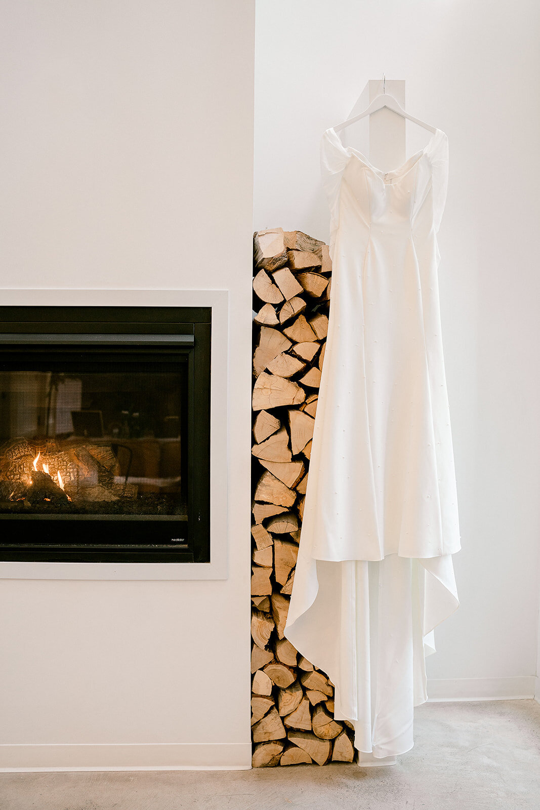 Wedding Dress hanging by a fireplace with firewood at Pinewood Wedding Venue