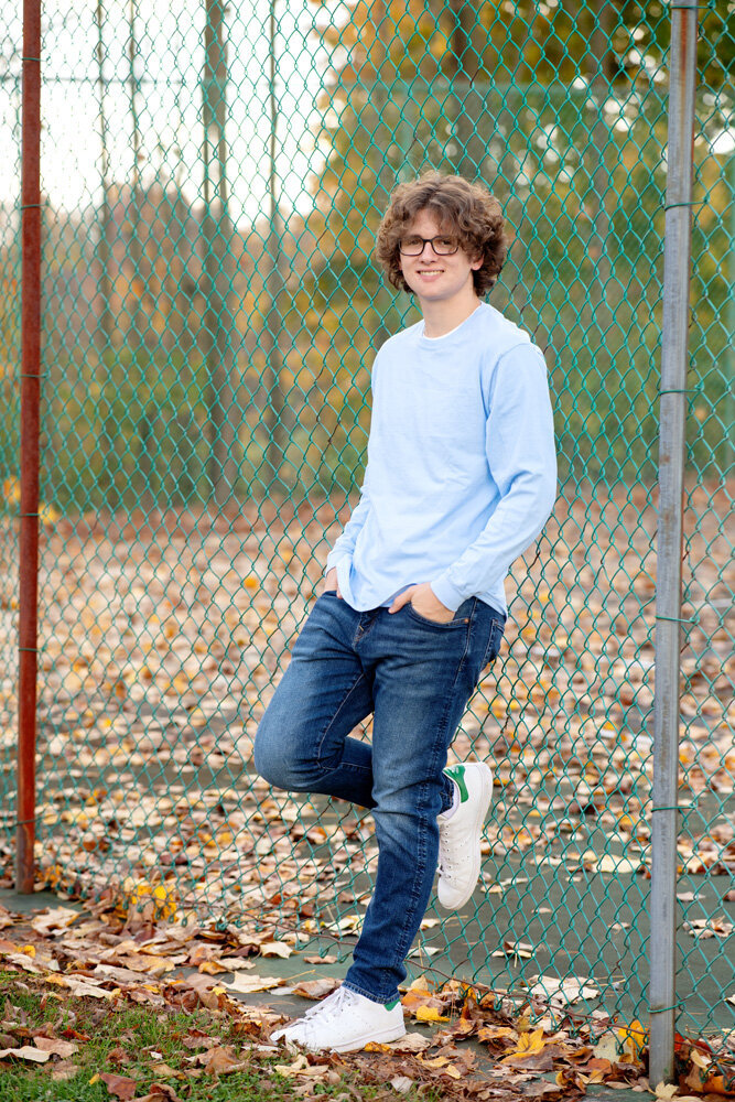 Senior session of a young man standing against a fence