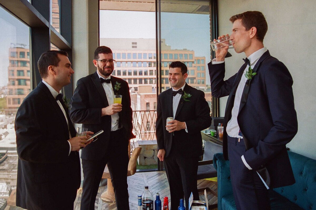 Groom and groomsmen standing together drinking.