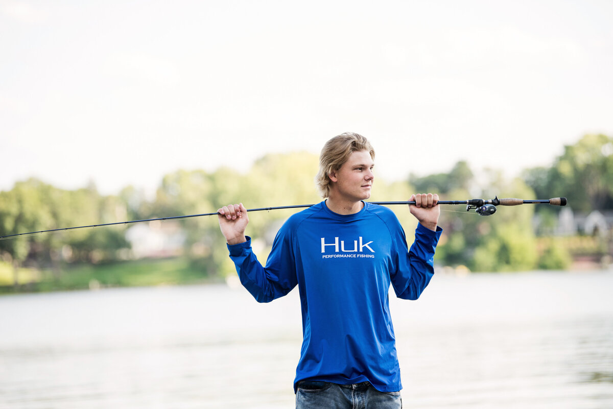 senior photo of boy with fishing rod on side of lake in minnesota