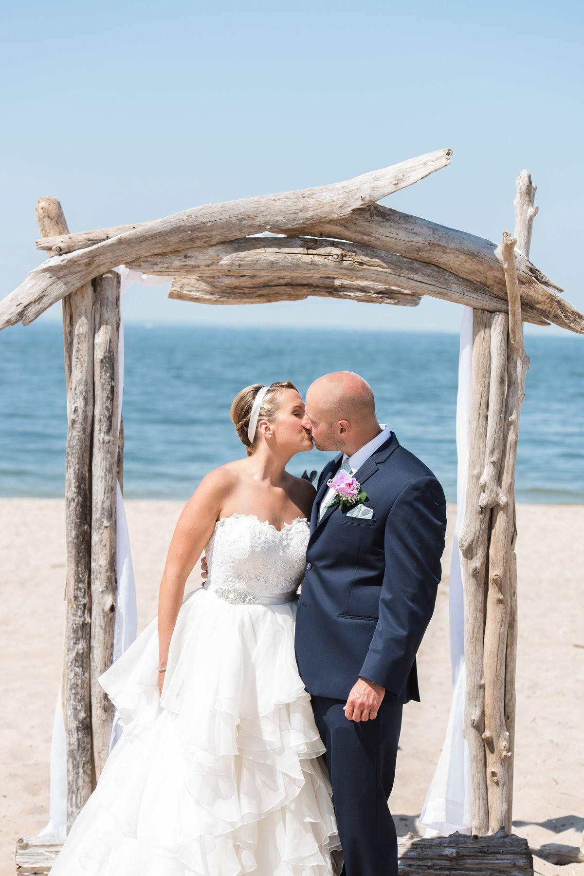 bride and groom kissing under ceremony arch on the beach from wedding at Pavilion at Sunken Meadow