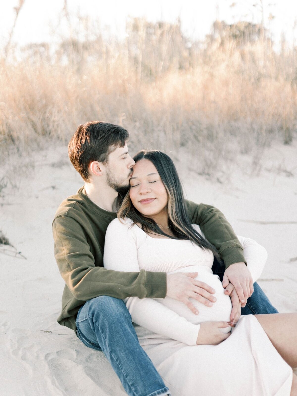 Man and pregnant women hug sitting on the beach.