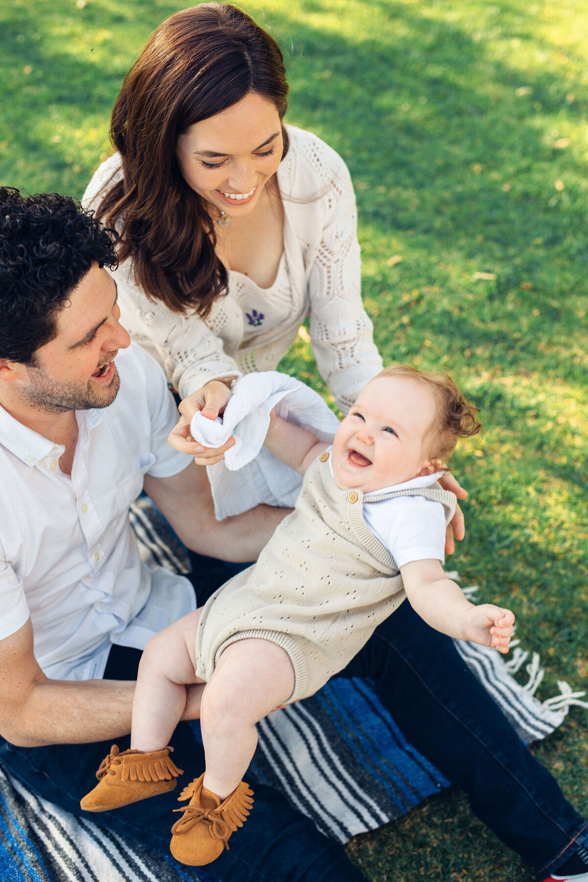 Family Portrait Photo Of Couple Playing With Their baby While Sitting On The Ground In Los Angeles