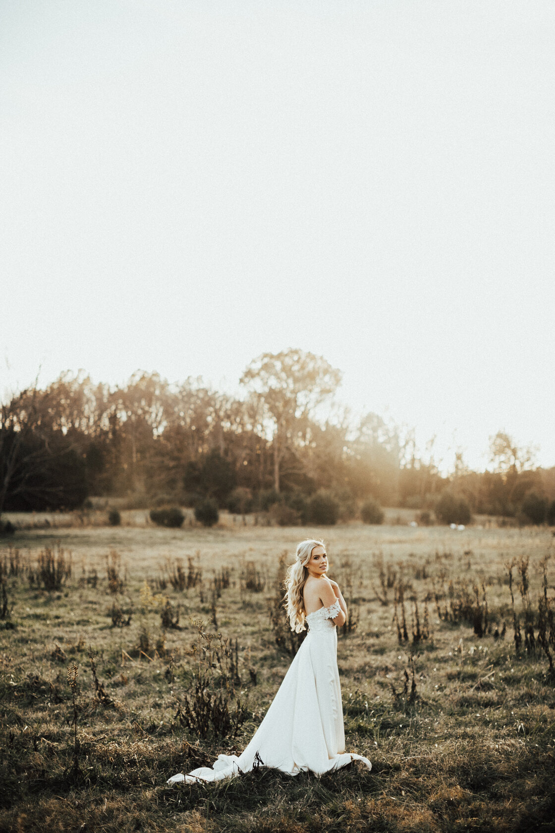 bride in wedding dress in a field at sunset