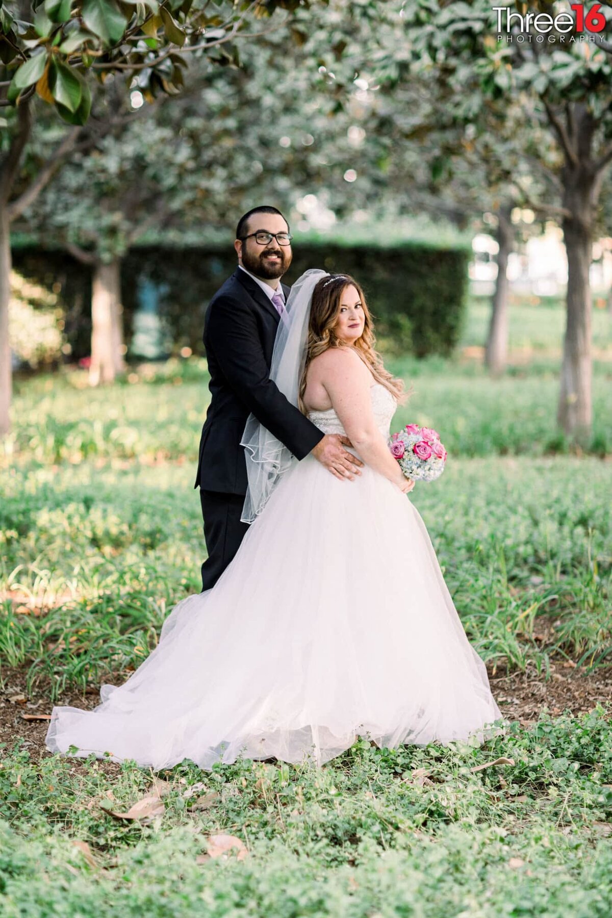 Groom poses up against his Bride from behind during their post wedding photo shoot