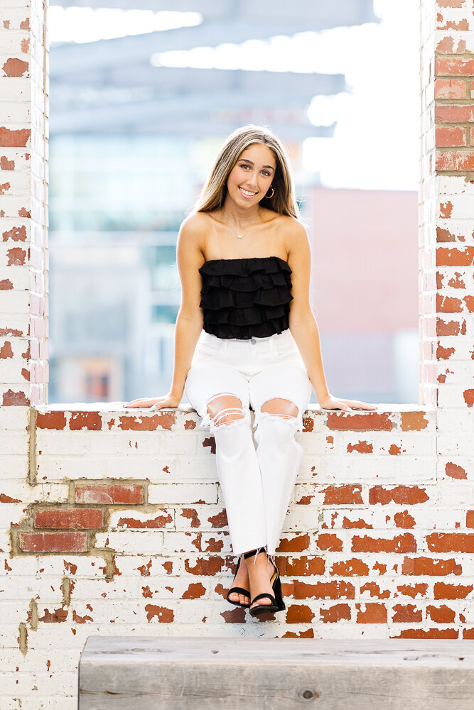 Senior girl sitting on a brick wall in downtown Raleigh.
