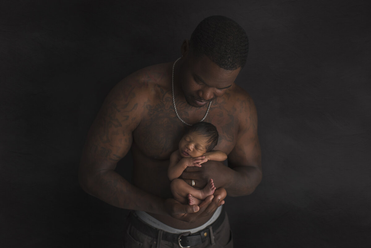 dad and newborn posed together in a dark theme