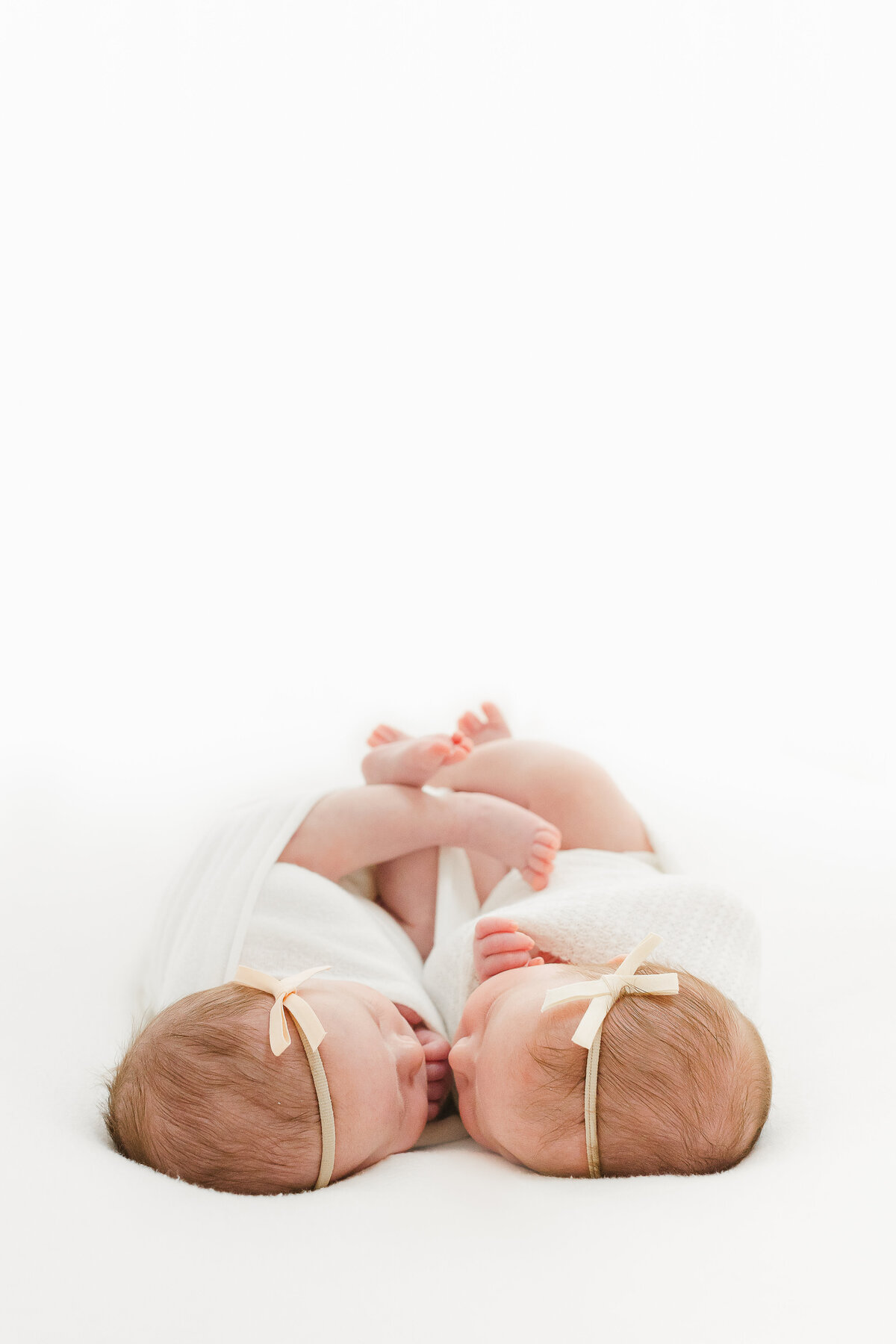 A photo of twin newborn baby girls snuggling nose to nose on a white blanket in front of a window by DC Baby Photographer