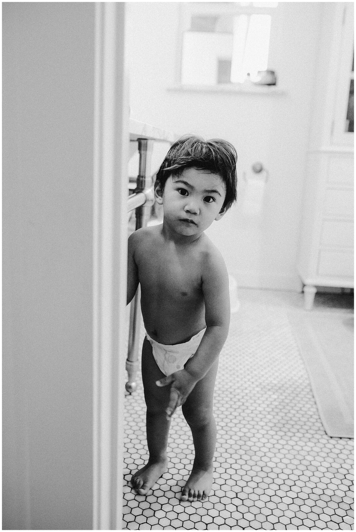Child in a diaper looking out from a bathroom at  family session at home in Austin Texas