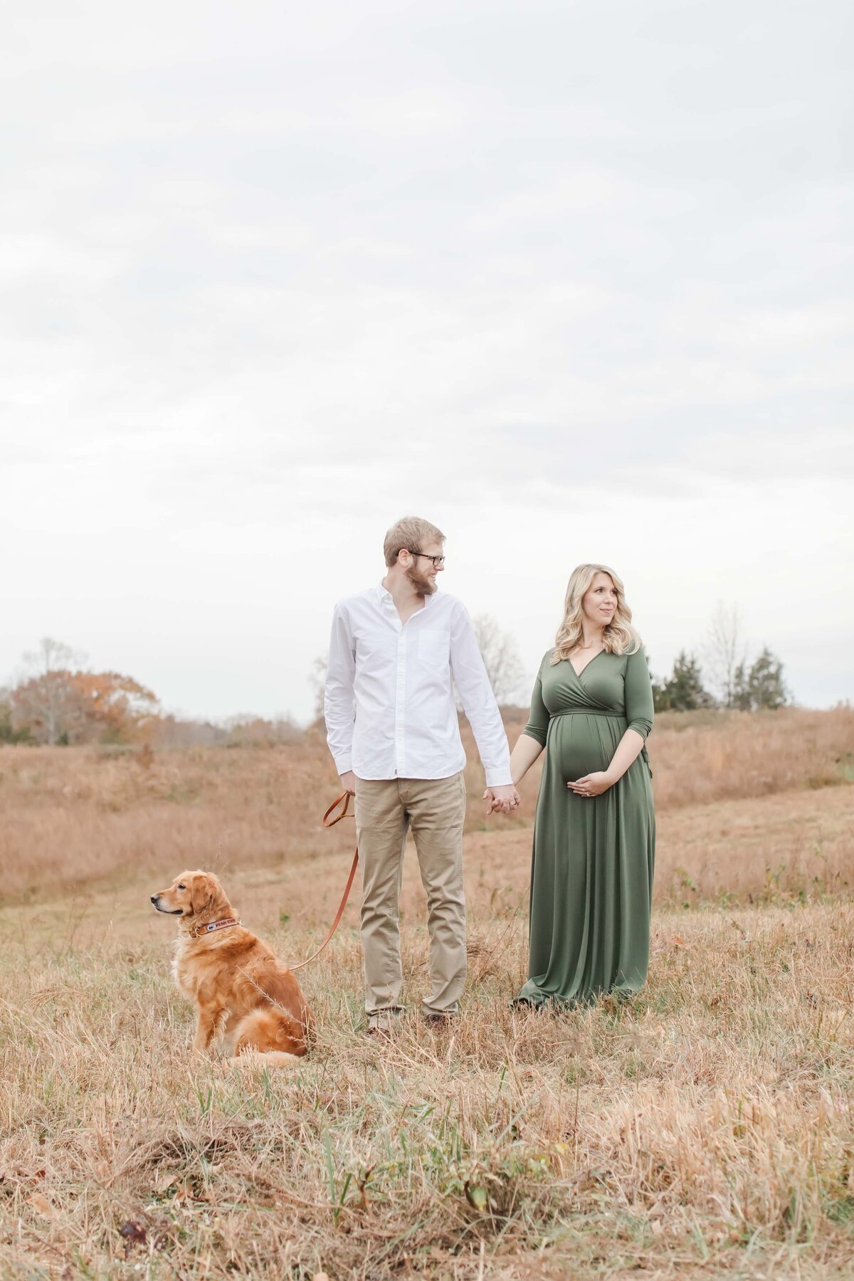 husband and wife holding hands during maternity photo session in Northern Virginia field with dog