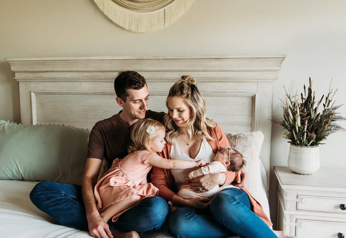 Newborn Photographer, Family of four kissing new baby on the bed.