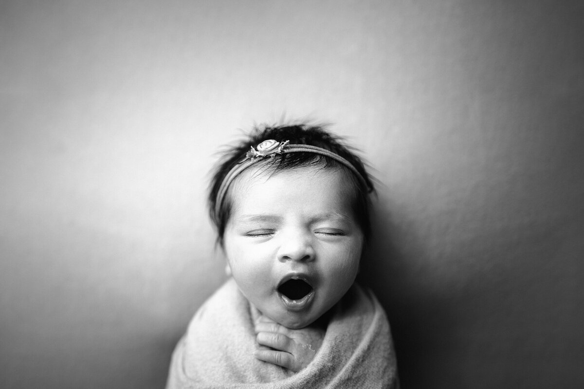 Black and white in home studio portrait of baby girl with rose headband yawning in Jacksonville, Florida.