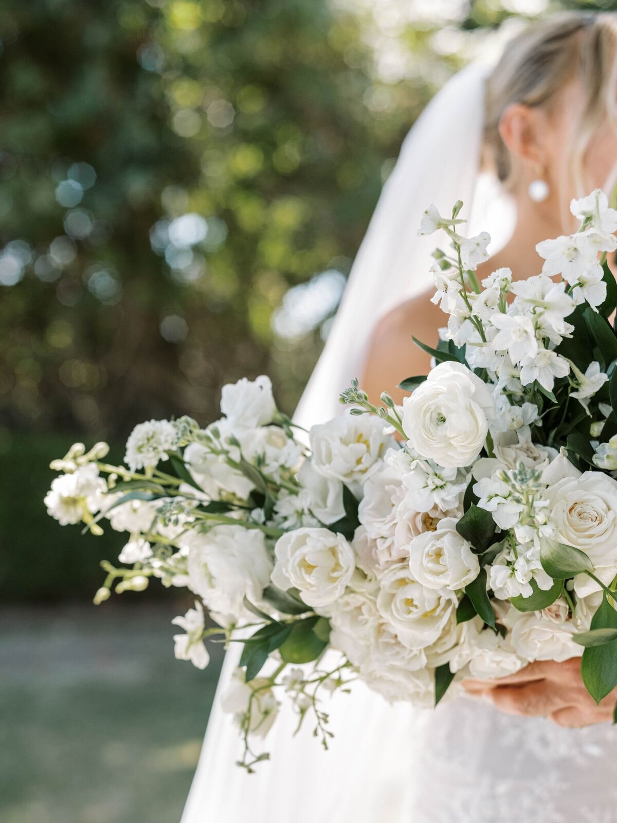 The bride holds a large white with green accent bouquet by Primrose and Petals.