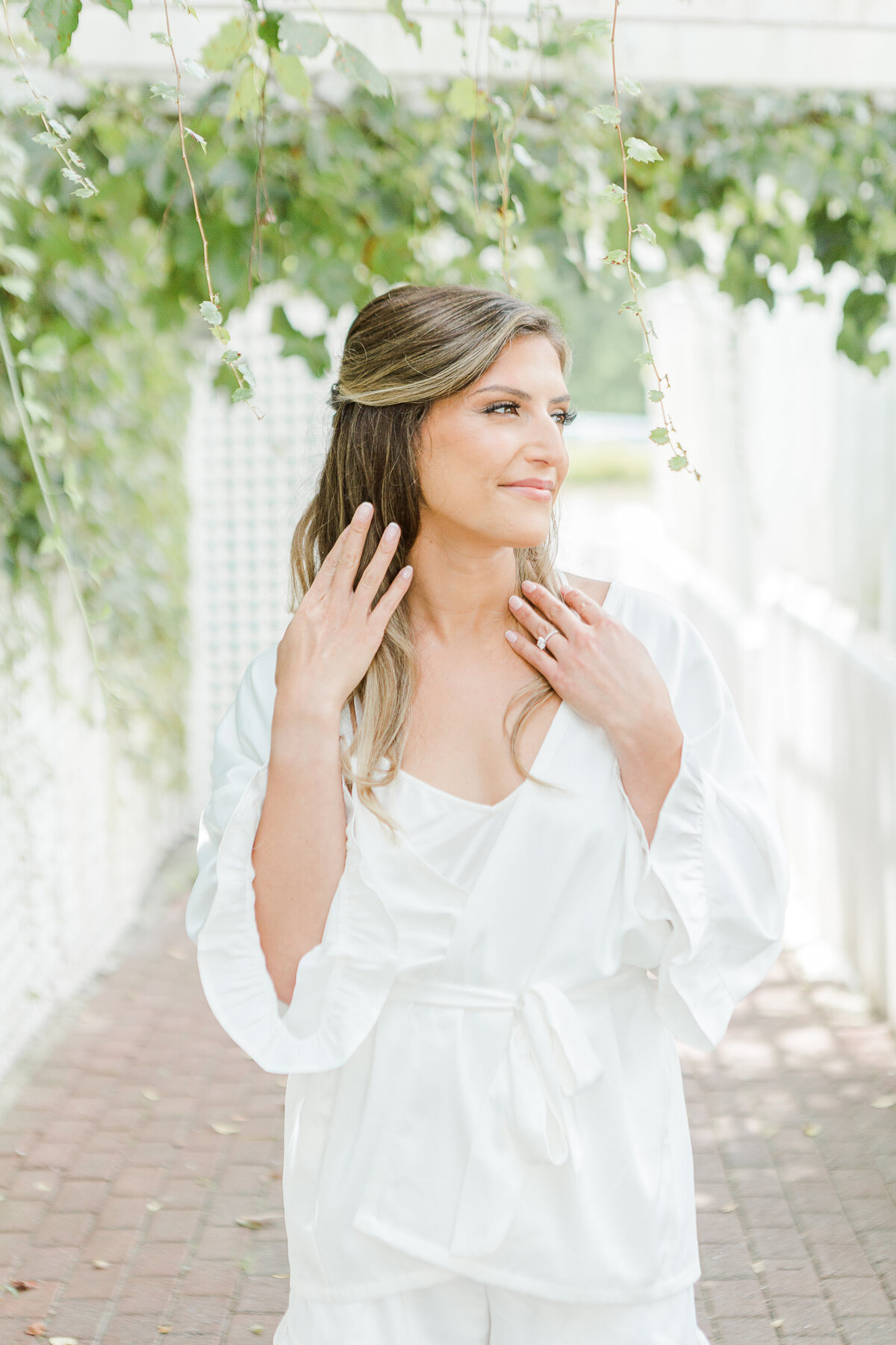 Bride poses for a getting-ready image at the Five Bridge Inn. She is wearing her bridal robe and looking off in the distance as she touches her hair. Captured by best Massachusetts wedding photographer Lia Rose Weddings.